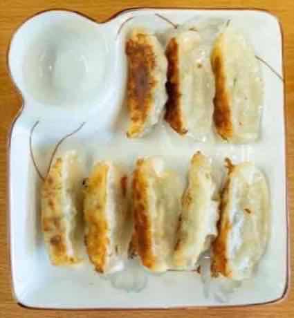 Plate of golden pan-fried pork dumplings with dipping sauce